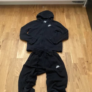 Svarta mjukisbyxor från Nike - Svarta mjukisbyxor från Nike med broderad vit logga på benet. Byxorna har resår och snörning i midjan för skön passform. Tillverkade i mjukt material som passar perfekt för chill eller träning.