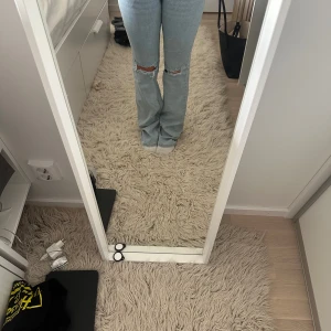 Ljusblå bootcut jeans med broderi - Säljer ett par ljusblå jeans med bootcut passform och slitningar vid knäna. Jeansen har snygga broderade detaljer i rosa och vitt på bakfickorna. De är midwaist och i klassisk denim med lite stretch. Perfekta för dig som gillar en avslappnad men trendig look.