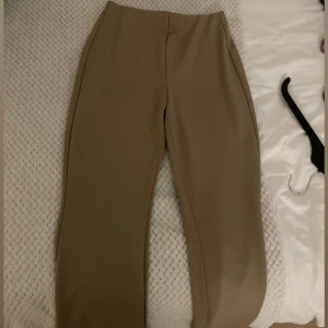 Beiga kostymbyxor med rak passform - Snygga beiga kostymbyxor med rak passform och minimalistisk design. Byxorna har hög midja och är tillverkade i ett mjukt, slätt material som ger en clean look. Perfekta för dig som gillar stilrena och klassiska vibes.