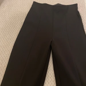 Svarta kostymbyxor med hög midja - Snygga svarta kostymbyxor med hög midja och raka ben. Byxorna har pressveck framtill för en clean och stilren look. Perfekta att styla med en oversized skjorta eller en tight topp.