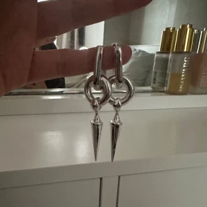 Unika coola örhängen med spets - Coola silvriga örhängen med chunky ring och hängande spetsig konformad detalj. Passar dig som gillar statement-smycken.