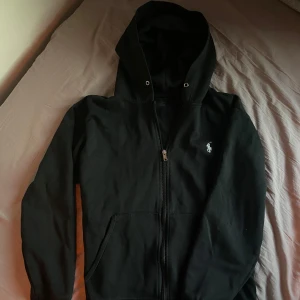 Svart hoodie från Ralph Lauren - Svart hoodie från Ralph Lauren med dragkedja och klassisk vit logga. Saknar dock snöre till luvan, har köpt den själv på Plick.