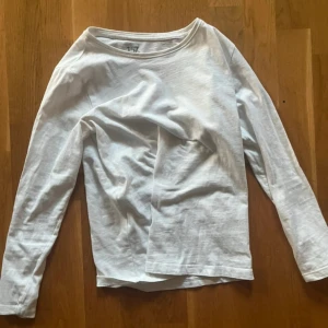 Vit långärmad tröja från 157 - En basic vit långärmad tröja från 157 i 100% bomull. Enkel och clean design med rund halsringning, perfekt att styla med jeans eller under en hoodie. Skön passform och mjukt material som funkar året runt.