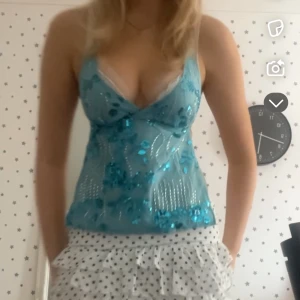 Turkos paljettlinnetopp med v-ringning - Supersnygg turkos linnetopp med v-ringning och tunna axelband. Toppen är dekorerad med glittriga paljetter och har en lätt transparent look. Perfekt för dig som vill sticka ut och få en riktig Y2K-vibe. Den är helt öppen i ryggen o man knyter runt halsen o runt ryggen jag råkade beställa tre av den så säljer två stycken helt oanvända