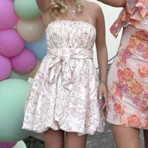 Ljus axelbandslös kortklänning med rosett - Jättesöt blommig klänning. Säljer på grund av för stor för mig…😊.