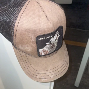 Brun keps Goorin Bros Lone Wolf - Snygg brun keps från Goorin Bros med svart mesh på baksidan och justerbar plastrem. Framtill finns ett broderat patch med en ylande varg och texten 'Lone Wolf'. Perfekt för dig som gillar djurmotiv och streetstyle. Den är inte bra skick den är solblekt. Kepsen är väldigt använd. Skriv vid minsta fråga 👍🏼☺️
