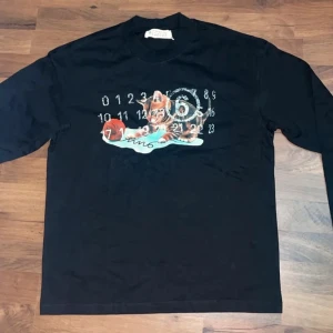 Svart Maison Margiela T-Shirt med tryck - Riktigt fet Maison Margiela t-shirt med tryck säljes, aldrig använd, storlek S | Skick: 10 / 10 | Nypris: 2800, se sista bilden | Vårt pris: 799 | Storlek: S | Tveka inte att höra av er med funderingar!