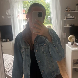 Klassisk ljusblå jeansjacka  - Säljer en klassisk ljusblå jeansjacka. Jackan har raka sömmar, silverfärgade knappar och två bröstfickor med lock. Materialet är äkta jeans och modellen är lite liten i passformen. Lite sliten men inget som gör att den ser ful ut.