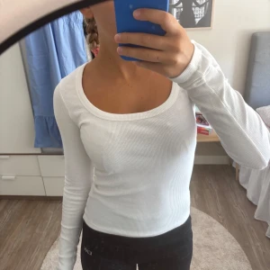 Vit ribbad långärmad topp - Säljer en likadan i svart!                            Superfräsch vit långärmad topp från Nelly med ribbad struktur och snygg, djup rundad urringning. Tight passform som sitter riktigt snyggt och är perfekt att styla med jeans eller kjol. Mjuk och stretchig bomullsmix som känns skön mot huden.