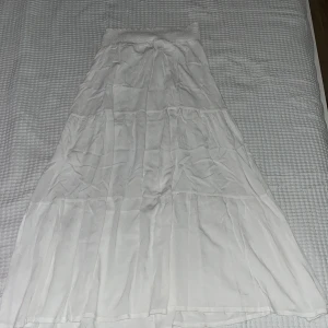 Vit långkjol från Lager 157 - Luftig och flowy vit långkjol från Lager 157 med smock i midjan för extra komfort. Kjolen har flera volanger och är perfekt för en chill och somrig vibe. Modellen heter BELLA och är lätt att matcha med crop tops eller oversized t-shirts.