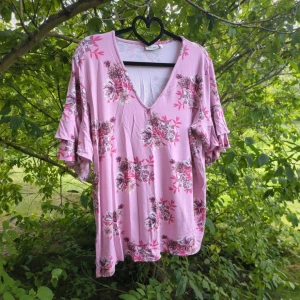 Blommig rosa blus från KappAhl - Säljer en söt rosa blus från KappAhl i storlek L med blommigt mönster i rosa, lila och beige toner. Blusen har v-ringad hals, volangdetaljer på de korta ärmarna och är gjord i mjuk bomull. Perfekt för dig som gillar romantiska vibes och vill ha något luftigt och bekvämt. Katter finns i hemmet.