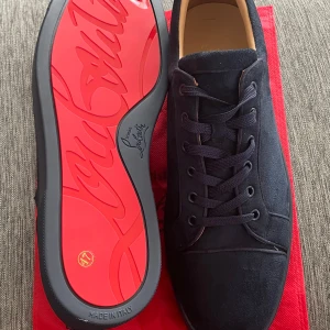 Svarta mocka sneakers från Louboutin 46/47 - Snygga svarta sneakers från Christian Louboutin i mjuk mocka med klassisk snörning och rund tå. Ikonisk röd sula med Louboutin-logga ger en lyxig vibe. Perfekta för dig som vill sticka ut med exklusiv stil och detaljer som verkligen syns. Priset är ej hugget i sten 
