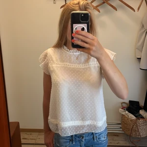 Vit prickig blus med volang från ONLY - Supersöt vit blus från ONLY i transparent tyg med små prickar, volangkant vid halsen och korta, luftiga ärmar. Säljer då den inte används💕