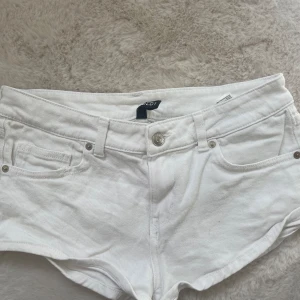 Vita lowwaist jeansshorts  - Snygga vita jeansshorts från Divided med klassisk femficksdesign och låg midja. De är tillverkade i bomull och har bälteshällor, knapp och dragkedja framtill. Perfekta för varma sommardagar och enkla att matcha med allt.