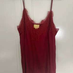 Vinrött spetslinne från H&M - Säljer ett vinrött linne från H&M med tunna axelband och vacker spetsdetalj vid urringningen och ärmhålen. Linnet har en mjuk, flowy känsla och är perfekt för dig som gillar romantiska vibes och en feminin look.