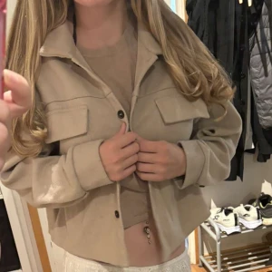 Beige overshirt med fickor - Snygg beige overshirt med krage och två stora bröstfickor. Jackan har knäppning framtill med svarta knappar och är i ett mjukt material som känns skönt mot huden. Perfekt nu till hösten. Storlek M, använd men som ny. 