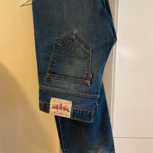 Levi's blå jeans straight  - Klassiska Levi's jeans i blå denim med raka ben och normal passform. Snygga slitningar och ikoniska bakfickor med den röda Levi's-taggen. Perfekta för dig som gillar tidlös stil och vill ha ett par jeans som funkar till allt.