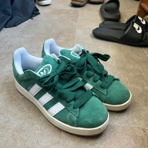 Adidas Campus gröna sneakers mocka - Gröna Adidas Campus sneakers i mocka med klassiska vita ränder och logga på hälen. Skorna har breda gröna skosnören, vit innersida och platt sula. Helt nya, använda endast två gånger. 