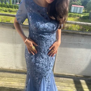 Vacker blå långklänning till bröllopet eller balen - Säljer en magisk blå långklänning med glittriga paljettdetaljer och bladmönster. Klänningen har korta ärmar och en passform som ger en elegant siluett. Den har en dragkedja i ryggen och är super lätt att dra på sig! Perfekt för bal eller fest! 🎉 Säljs då jag redan hade en balklänning tyvärr🥰