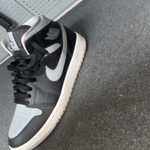 Nike Air Jordan 1 svart/grå sneakers - Snygga Nike Air Jordan 1 sneakers i svart och grått med klassisk vit sula. Skorna har högt skaft, svart snörning och ikoniska Air Jordan-loggan på sidan. Tillverkade i skinn med perforerad tå för extra ventilation. Säljer endast för 950kr köptes 1200kr priset kan diskuteras vid snabb affär skriv gärna för frågor!