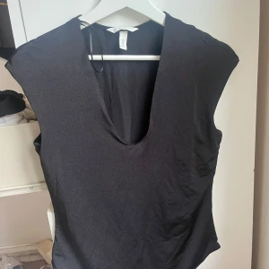 Svart body med djup v-ringning - Svart ärmlös body från H&M med djup v-ringning. Snygg och enkel design som passar perfekt till jeans eller kjol. Tillverkad i mjukt och stretchigt material för en bekväm passform.