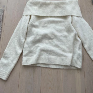 Offshoulder stickad vit tröja - Superfin offshoulder stickad tröja i vit färg med bred ribbad kant upptill och vid ärmslut. Perfekt för dig som vill ha en stilren och trendig look med en twist. Snygg att styla med jeans eller kjol för en chill vibe.