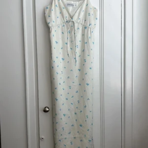 Vit långklänning med blå blommor från Adoore - Superfin långklänning från Adoore i vit med små blå blommor. Klänningen har v-ringning, smala axelband och en söt knytning under bysten. Materialet känns lätt och luftigt, perfekt för varma dagar.  Endast provad 