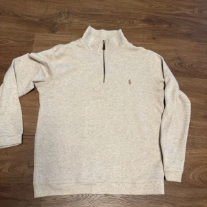 Beige half zip tröja från Polo Ralph Lauren - Snygg beige långärmad tröja från Polo Ralph Lauren med half zip och liten broderad logga på bröstet. Tröjan har en hög krage och är gjord i mjuk bomull, perfekt för chill dagar. Enkel och stilren design som funkar till jeans eller sweatpants.