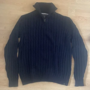 Marinblå stickad tröja med half zip - Säljer en marinblå stickad tröja från Indicode i storlek medium. Tröjan har ett snyggt kabelstickat mönster, hög krage och half zip-dragkedja framtill. Tillverkad i 100% bomull, perfekt för kyliga dagar. Långärmad och riktigt skön att bära. Använd 1 gång