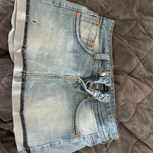 Ljusblå jeanskjol  - Snygg kjol med klassiska fem fickor, slitna detaljer och kontrastsömmar. Kjolen har låg midja och råa kanter nertill för en avslappnad vibe. Perfekta för varma dagar och enkel att matcha med allt.