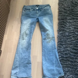 True Religion Joey Low Rise Flare Jeans - Säljer ett par ljusblå True Religion Joey jeans med låg midja och flare-ben. Klassiska kontrastsömmar, snygga bakfickor med lock och silverfärgade knappar. 
