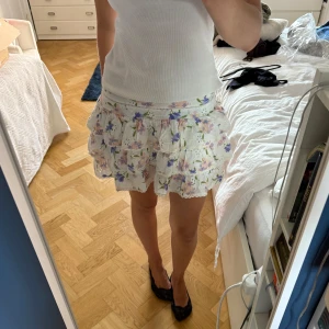 Blommig volangkjol från Zara - Supersöt kort kjol från Zara med volanger och blommigt mönster i lila, rosa, grönt och vitt. 