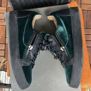 Giuseppe Zanotti sneakers i grön sammet - Unika sneakers från Giuseppe Zanotti i mörkgrön sammet med svarta detaljer i skinn. Skorna har kraftig platt sula, snörning och dragkedjor på sidorna för extra edge. Perfekta för dig som vill sticka ut med lyxig streetstyle.