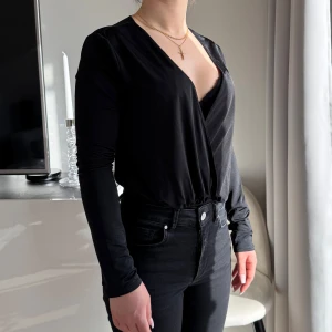 Svart body - Säljer min body i strl XS. Köpt från Nelly, knappt använd. Har använt säkerhetsnål för att minska v-ringningen. Den öppnas enkelt av rörelser.