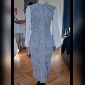 Grå ribbad klänning från Shein - Snygg grå ribbad klänning från Shein med vita långa ärmar och dekorativa guldknappar vid axlarna. Klänningen har en tight passform och är perfekt för en stilren look.