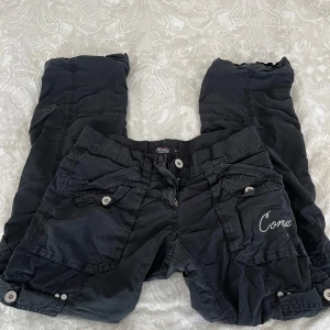 Svarta cargobyxor med knappar - Snygga svarta cargobyxor med flera fickor och knappdetaljer. Storlek 164 men passar XS/liten S, kom med prisförslag. Finns en liten fläck på knät men vet inte om det försvinner i tvätten 