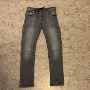 Grå jeansbyxor från LAB Industries - Snygga grå jeansbyxor från LAB Industries med en modern look. Byxorna har en dragsko i midjan för extra komfort och stil. Perfekta för en avslappnad vardagsstil.