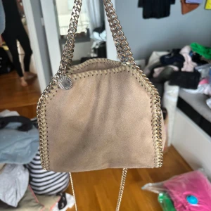   Stella McCartney väska mini med guld kjedja - Väska från Stella McCartney modellen mini med guldig kjedja. Bra skick. Köpt av en kompis till mig. Har inget kvitto tyvärr men den är äkta! Är mest intresserad av att byta! Helst mit en svart med guldig kjedja. Kan kanske tänka mig sälja men beror på❤️❤️❤️❣️❣️