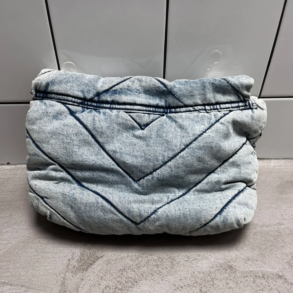 Snygg quiltad axelväska i ljusblått jeansmaterial med kedjerem. Väskan har ett stilrent spänne framtill och ett mjukt, vadderat utseende. Perfekt för att ge din outfit en cool touch.. Laukut & Käsilaukut.