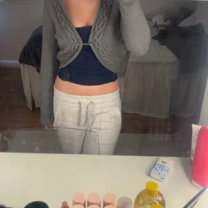 Grå stickad kofta - Säljer en grå stickad kofta med knytning framtill. Koftan har ett flätat mönster och långa ärmar. Perfekt för att hålla sig varm och stilren. Målen man stänger själva koftan med går o ta bort också.