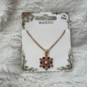 Guldhalsband med snöflingehänge från Montini - Elegant guldhalsband från Montini med ett snöflingeformat hänge dekorerat med röda och gröna stenar samt en vit pärla i mitten. Perfekt för att ge en festlig touch till din juloutfit. Aldrig använt🤍