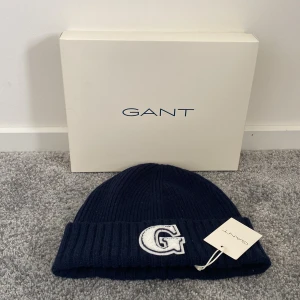 Mörkblå mössa från GANT - Helt ny mörkblå mössa från GANT med en stor broderad bokstav 'G' framtill. Tidigare pris 959kr. Perfekt för att hålla värmen under kyliga dagar. Mössan har en ribbad design som ger en skön passform. Size: ONE SIZE 