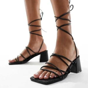 Svarta sandaler med klack  - Snygga svarta sandaler med klack och smala remmar som knyts runt ankeln. Perfekta för en stilren look. (Oanvända i nytt skick)