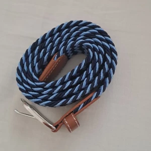 Blått flätat bälte med bruna detaljer - Snyggt flätat bälte i blått med bruna läderdetaljer och silverfärgat spänne. Perfekt för att ge en stilren touch till din outfit. Bältet har en unik flätad design som ger det en modern känsla.