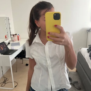 Vit kortärmad blus - Säljer en stilren vit blus med korta ärmar och knappar framtill. Perfekt för en fräsch och klassisk look. Blusen har en krage och är lätt figursydd för en smickrande passform.