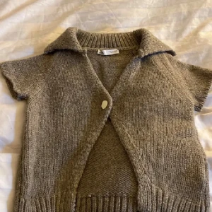 Beige stickad väst med krage - Säljer en mysig beige stickad väst från Lindex. Västen har en stor krage och stängs med en knapp framtill. Perfekt för lager-på-lager under kyligare dagar.