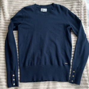 Mörkblå tröja från Lindex - Snygg marinblå finstickad tröja från Lindex med långa ärmar och dekorativa guldiga knappar vid ärmsluten. Perfekt för en stilren look. Tröjan har en ribbad nederkant. Det finns små slitningar på knapparna, men det är inget som märks!!💗Perfekt nu inför skolstart och hösten🫶🏼