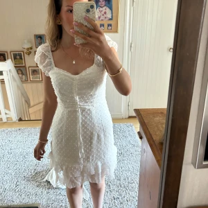 student klänning - Säljer en söt vit klänning med prickigt mönster och volangdetaljer. Klänningen har korta ärmar och en v-ringad design. Perfekt för sommarens alla tillfällen! 💫