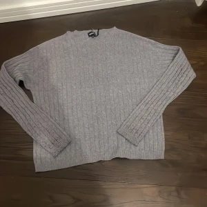 Grå stickad tröja från RVLS - Säljer en stilren grå tröja i merinoull från RVLS. Tröjan har ett klassiskt kabelstickat mönster och långa ärmar. Perfekt för kyligare dagar. 🧶Hör av er vid frågor!