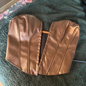 Brun korsett i skinnimitation - Snygg brun korsett i skinnimitation med hakknäppning framtill. Perfekt för en stilren look med en touch av edge.